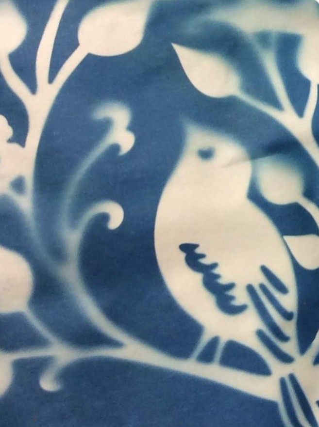 A cyanotype print in which the characteristic deep blue background contrasts with an image of a small bird sitting on a tree.  